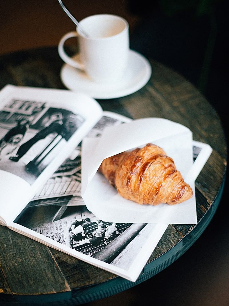 Croissant e café em uma mesa com uma revista aberta.