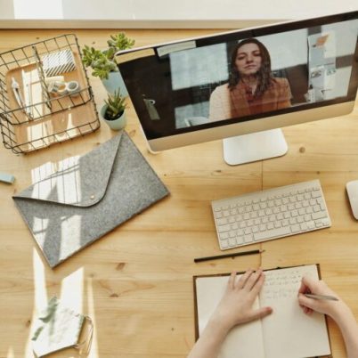 Person taking notes during a video call at a neatly organized home desk, showing remote work lifestyle.